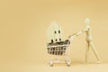 Wooden mannequin or puppet pushing shopping cart with wooden house and coins money on orange background Royalty Free Stock Photo