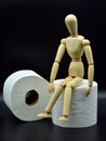 Wooden mannequin sitting on a roll of toilet paper