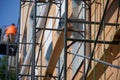 Wooden and metal scaffolding next to the exterior wall and windows of a multi-story building. Working plasterer-high-rise worker