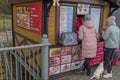 Wooden mini-fast food store, on walls hang menus, woman in pink jacket makes order, girl in lime green jacket with dog waiting