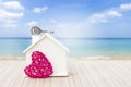 Wooden model house with key and pink wooden heart over blurred beach background, summer house Royalty Free Stock Photo