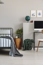 Wooden nightstand with spruce in glass vase and clock in grey kid`s bedroom interior with copy space on the empty grey wall