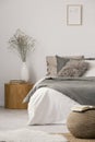 Wooden nightstand table next to king size bed with white and grey bedding in simple bedroom interior Royalty Free Stock Photo