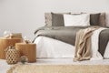 Wooden nightstand table next to king size bed with white and grey bedding in simple bedroom interior
