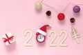 Wooden numbers 2022 on a pink background with a Christmas tree, gifts, a garland and an alarm clock in a Santa Claus hat. It`s Royalty Free Stock Photo