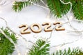 Wooden numbers 2022 silhouette with green fir tree branches and lights on light background. New Year beginning congratulations Royalty Free Stock Photo