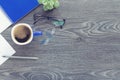 For design wooden office desk table with notebook, glasses, plant, blue cup of coffee and other office supplies. Top view with cop