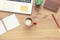 For design wooden office desk table with notebook, laptop, glasses, plant, red cup of cappuccino and other office supplies. Top vi