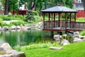 Wooden openwork arbor on stilts over the water of a forest lake, surrounded by a beautiful park with landscaping Royalty Free Stock Photo