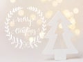 Wooden ornament fir tree in forest golden bokeh garland lights white background. Greeting card with Merry Christmas lettering Royalty Free Stock Photo