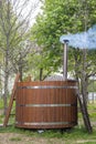 A wooden outdoor bath font stands on the grass in the courtyard. Concept: sauna and steam room, outdoor water treatments, NATURAL