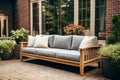 Wooden outdoor couch with blue and white textile cushions. Green potted plants. Georgian style residential house wall in the