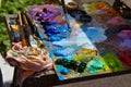 Wooden palette, mess of fresh bright colorful oil paints mixed in disorder, outdoor painting plein air, inspiration postcard Royalty Free Stock Photo