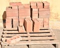 a wooden pallet plenty of old stacked red bricks in rows. Behind there is other pile of red bricks wrapped with plastic Royalty Free Stock Photo