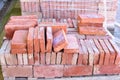 a wooden pallet plenty of old stacked red bricks in rows. Behind there is other pile of red bricks wrapped with plastic. Royalty Free Stock Photo