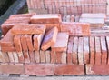 a wooden pallet plenty of old stacked red bricks in rows. Behind there is other pile of red bricks wrapped with plastic. Royalty Free Stock Photo