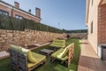 Wooden pallet sofa with green cushions and matching coffee table next to a brick house with a garden, artificial grass floor and Royalty Free Stock Photo