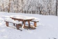 Wooden park bench and table covered with snow with frozen forest Royalty Free Stock Photo