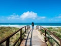 A wooden path leading to the beach, in the background a woman walking towards the sea, in the wild nature