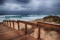 Wooden pathway on the beach by the breathtaking ocean waves under the cloudy sky Royalty Free Stock Photo