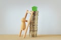 Wooden pawn climbing a ladder to reach a little green house on top of coin tower - Concept of buying home Royalty Free Stock Photo