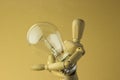 Wooden person holds electric bulb in hand