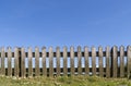 Wooden picket fence with grass, daisies and blue summer sky behind. Unpainted, natural wood. Royalty Free Stock Photo