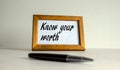 Wooden picture frame with inscription `know your worth` on beautiful white background. Pen on the table. Concept