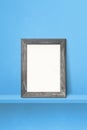 Wooden picture frame leaning on a blue shelf. 3d illustration. Vertical background Royalty Free Stock Photo