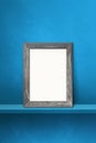 Wooden picture frame leaning on a blue shelf. 3d illustration. Vertical background Royalty Free Stock Photo