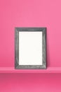 Wooden picture frame leaning on a pink shelf. 3d illustration. Vertical background Royalty Free Stock Photo