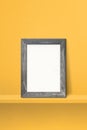 Wooden picture frame leaning on a yellow shelf. 3d illustration. Vertical background Royalty Free Stock Photo