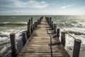 A wooden pier extends into a turbulent sea under a partly cloudy sky, evoking feelings of solitude and tranquility despite the