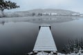 Wooden pier on lake covered with fresh snow.Winter pond with small jetty on misty morning.Foggy cloudy landscape reflected in Royalty Free Stock Photo