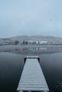 Wooden pier on lake covered with fresh snow.Winter pond with small jetty on misty morning.Foggy cloudy landscape reflected in Royalty Free Stock Photo