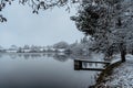 Wooden pier on lake with fresh snow.Winter pond with small jetty on misty morning.Foggy cloudy landscape reflected in water. White Royalty Free Stock Photo