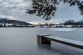 Wooden pier on lake with fresh snow.Winter pond with small jetty at sunrise,village in backround.Frosty calm landscape. White Royalty Free Stock Photo