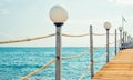 Wooden pier with lamp and cord railing against blue sky and sea background. Tropical landscape Royalty Free Stock Photo