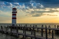 A wooden pier leading to the lake and a red and white lighthouse on Lake Neusiedl in Podersdorf, Austria. In the background is a Royalty Free Stock Photo