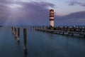 A wooden pier leading to the lake and a red and white lighthouse on Lake Neusiedl in Podersdorf, Austria. In the background is a Royalty Free Stock Photo