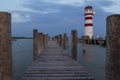 A wooden pier leading to the lake and a red and white lighthouse on Lake Neusiedl in Podersdorf, Austria. In the background is a Royalty Free Stock Photo