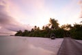 Wooden pier with lights into paradise island in Maldives. Sunset beach landscape, high key bright sky calm sea water Royalty Free Stock Photo