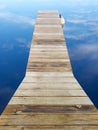 Wooden pier ponton wood jetty in blue water reflection mirror image sky cloudy day Royalty Free Stock Photo