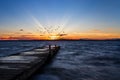 Wooden pier in the sea with a flock of birds flying in the sunset sky in the horizon