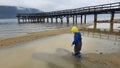 wooden pier for ships in rainy weather river shore and a little boy in a yellow cap
