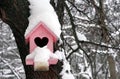 A Wooden Pink Birdhouse With A Heart-shaped Entrance With Snow
