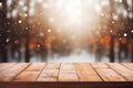 Wooden planks table on winter frosty forest trees background with blurry snowflakes in sunlight