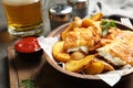 Wooden plate with British traditional fish and potato chips on table. Royalty Free Stock Photo