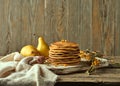 A wooden plate with classic American pancakes on it, two pears in the background, a sprig of sea buckthorn, and a spoon for honey