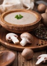 Wooden plate of creamy chestnut champignon mushroom soup with wooden spoon, pepper and kitchen cloth on wooden background Royalty Free Stock Photo